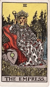The Empress reclines on cushions in a lush field of wheat, a crown of twelve stars on her head and a Venus-marked shield beside her.