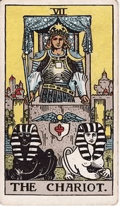 An armored figure rides The Chariot, drawn by a black sphinx and a white sphinx with no visible reins between them.